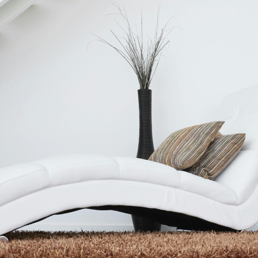 Elegant white lounge chair with cushions on plush carpet, perfect for relaxation.